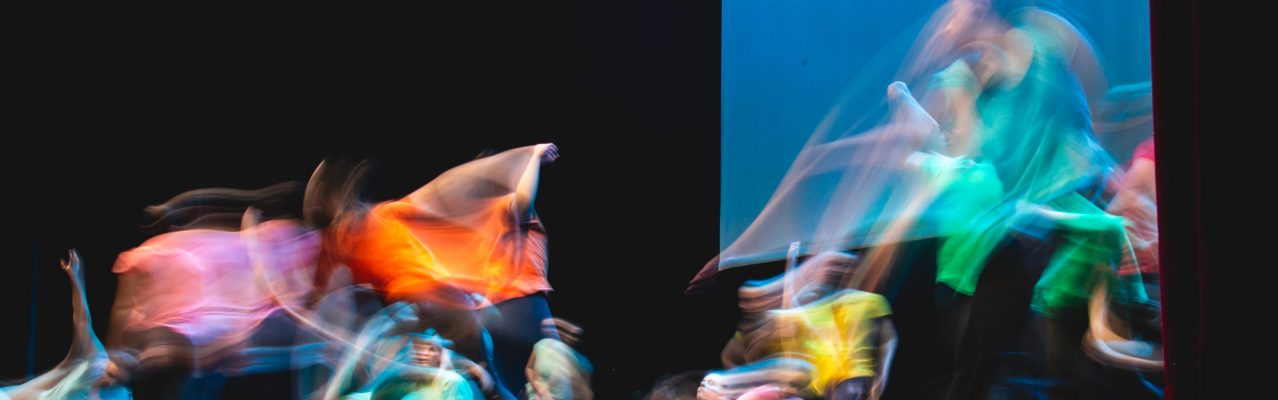 Group of dancer in colored clothes dancing on the stage in long exposure. Dark background